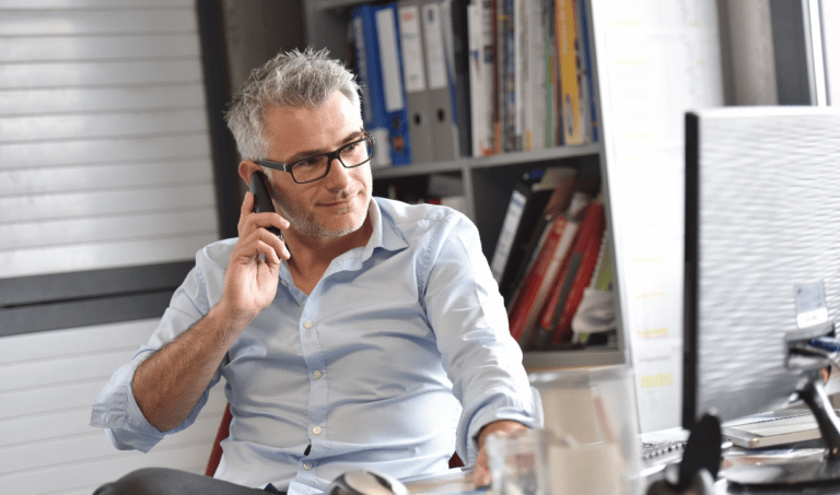 Man sitting at office desk looking at laptop while talking on a cell phone