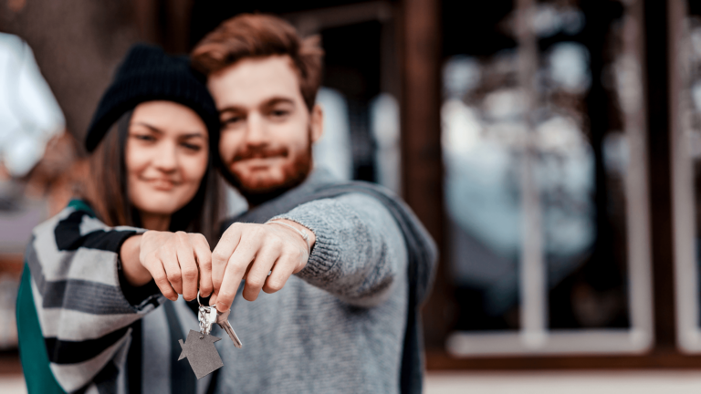 A young couple in front of their new house holding a pair of keys